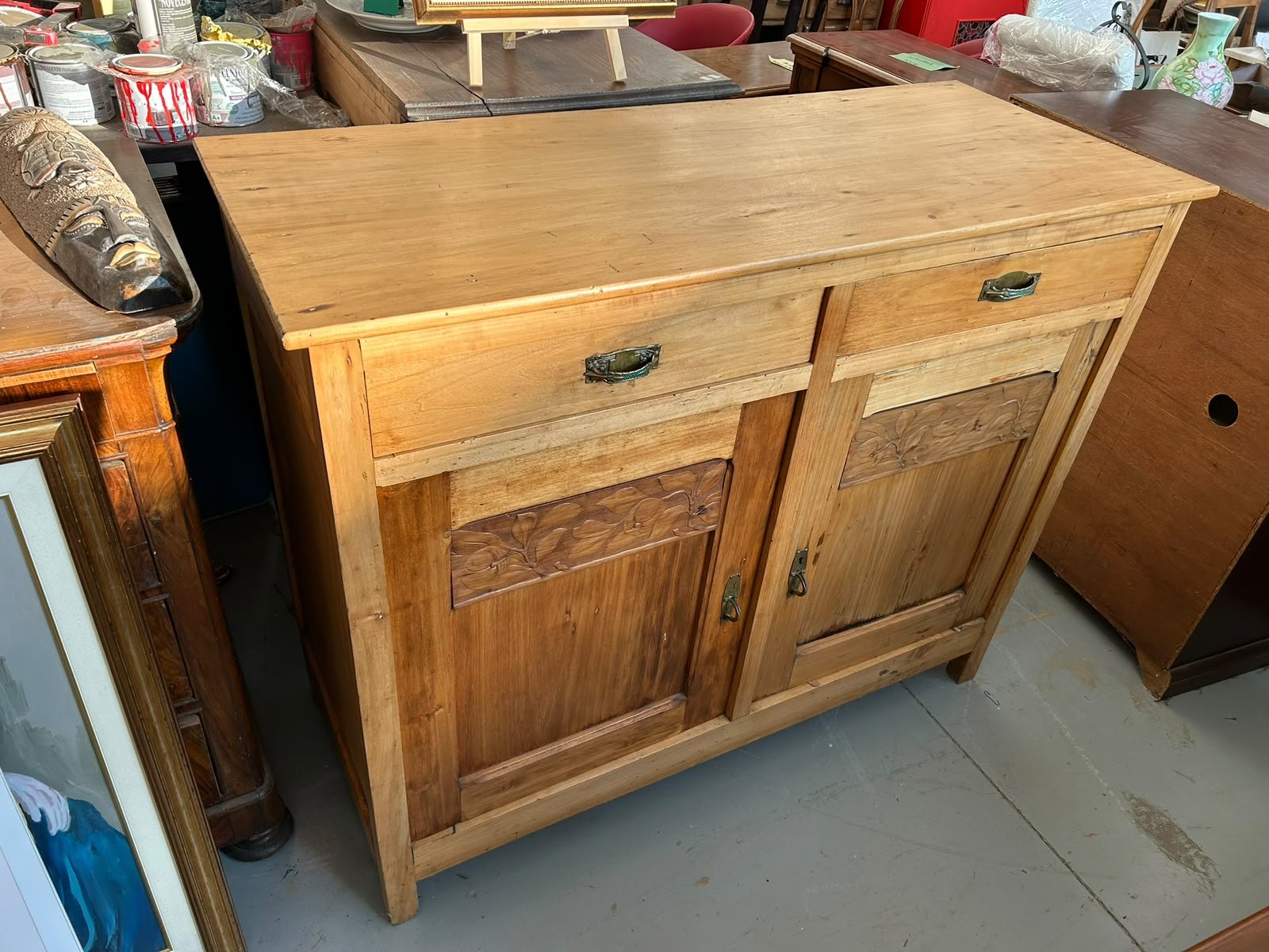 Credenza in legno chiaro con intagli floreali esposta tra gli altri arredi del negozio
